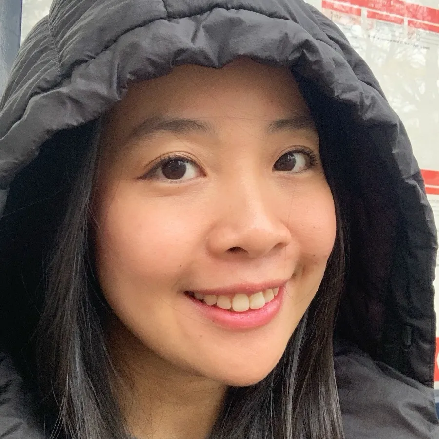 Lan Anh Dang smiling in a hooded jacket at a bus stop in the UK